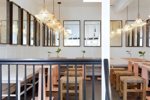 A modern interior with wooden tables and chairs, hanging woven light fixtures, and large mirrors on the walls.