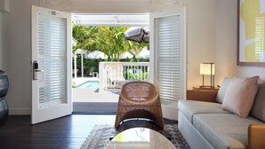 An open door leading to a pool area with a wicker chair and a sofa inside a room with a view of the pool. - Ella's Cottages - Key West Historic Inns (Key West)