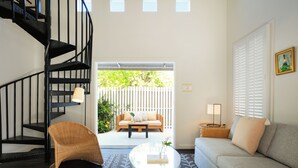 A living room with a spiral staircase, a sofa, a chair, a coffee table, and a view of an outdoor seating area. - Ella's Cottages - Key West Historic Inns (Key West)