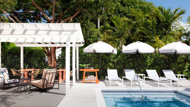 A poolside area with lounge chairs, umbrellas, and a pergola. - Ella's Cottages - Key West Historic Inns (Key West)
