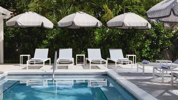 Un espace piscine agrémenté de chaises longues blanches et de parasols, le tout entouré d’une végétation luxuriante.