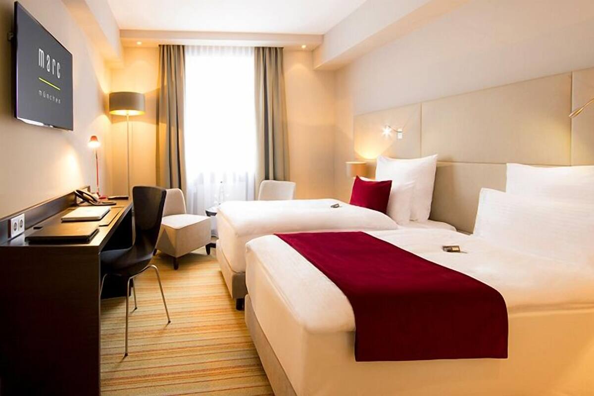 A hotel room with two beds, a desk, a chair, and a TV.