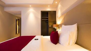 Habitación de hotel con una cama grande, un cojín rojo, una lámpara de noche y un armario.