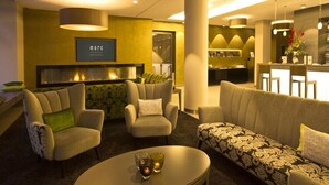 A modern lobby with a sofa, armchairs, a coffee table, and a bar area. - marc münchen - Adults Only (Munich)