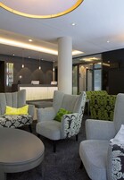Un vestíbulo moderno con sillones tapizados de gris, un mostrador de recepción y una mesa redonda.
