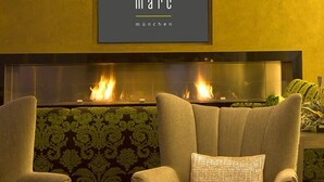 A modern lounge area with two armchairs, a round table with candles, and a fireplace with a visible fire. - marc münchen - Adults Only (Munich)