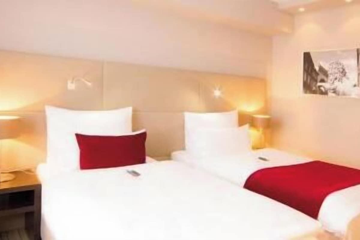 Une chambre d’hôtel avec deux lits, une table de chevet, une lampe et un tableau encadré au mur.