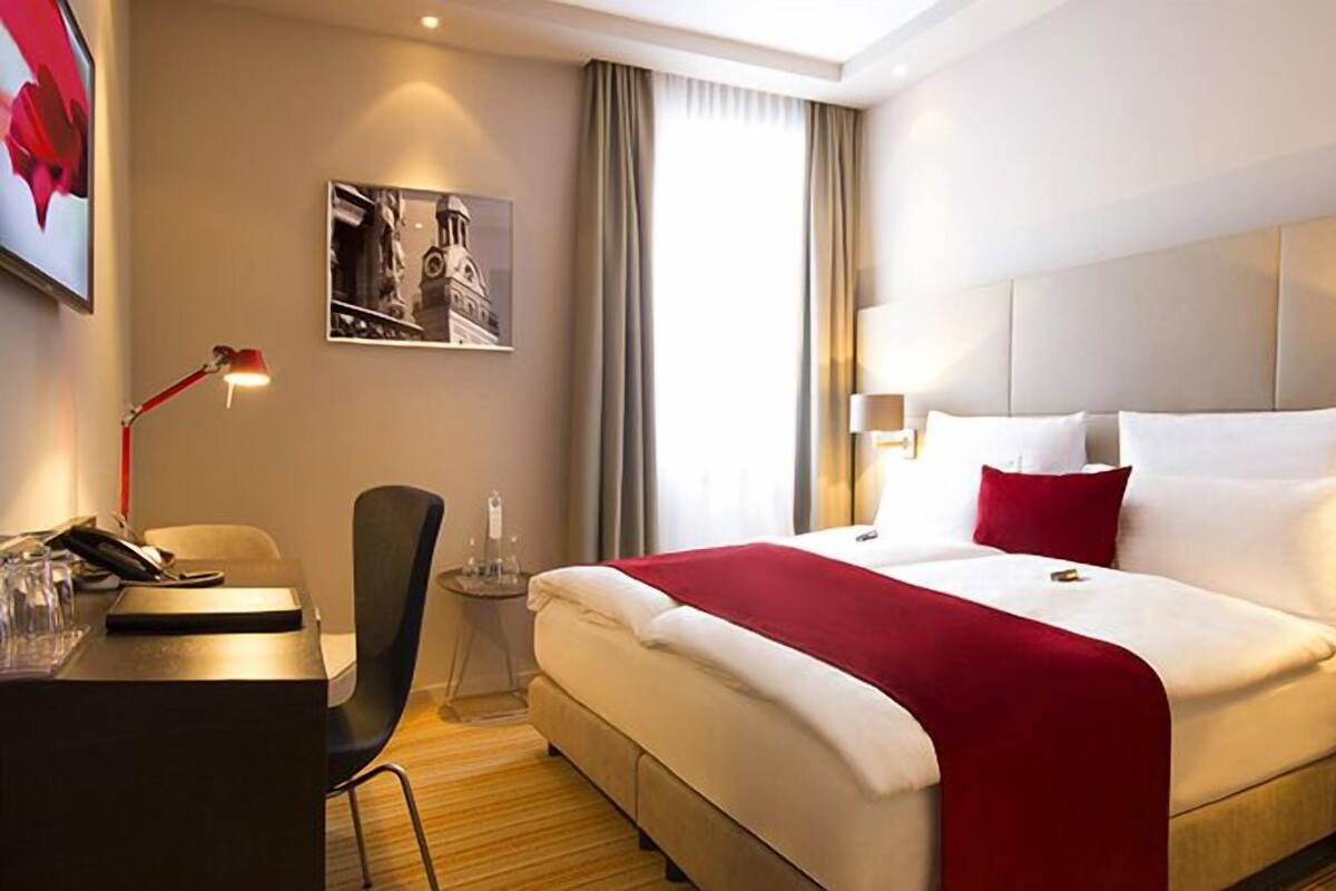 A hotel room with a bed, bedside tables, a desk, a chair, a lamp, and a picture on the wall.
