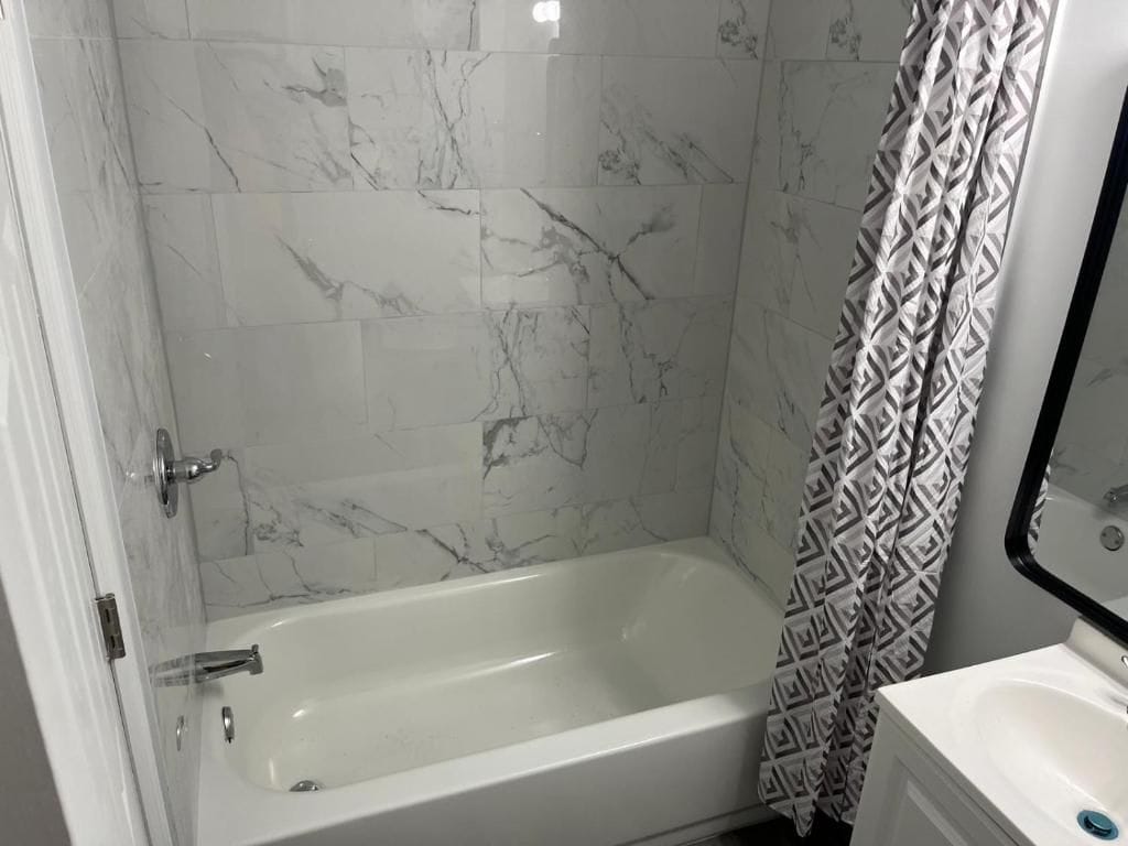 A bathroom with a bathtub, a shower curtain, and a sink.