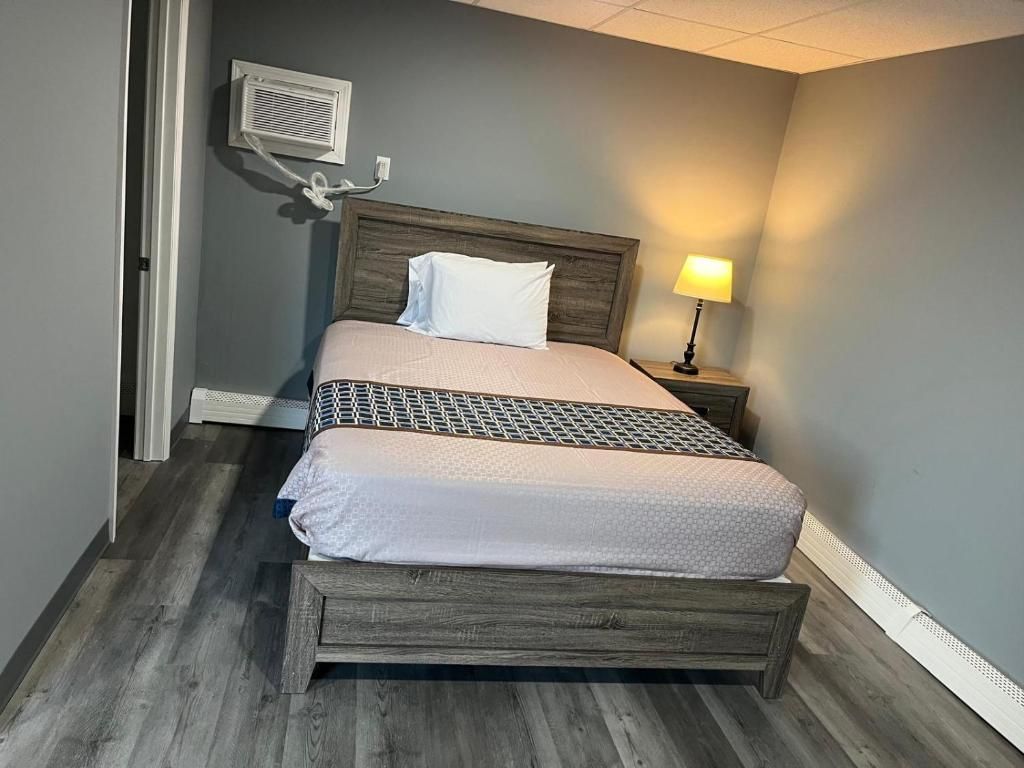 A single bed with a wooden frame, a white pillow, and a patterned bedspread in a room with grey walls and a wooden floor.