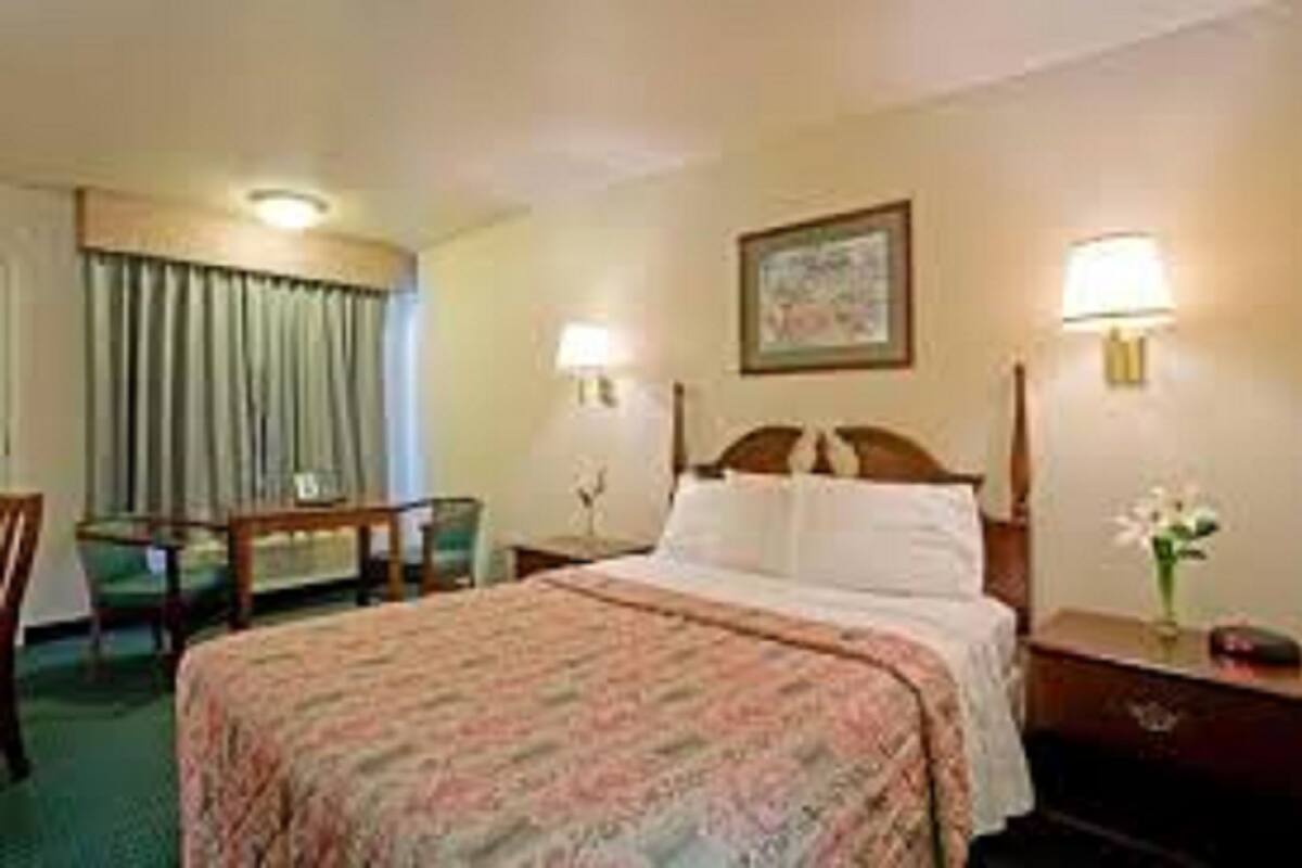 A hotel room with a bed, a desk, a chair, and two bedside lamps.