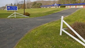 Ein Weg führt zu einem Gebäude mit blauem Dach, umgeben von grünem Gras und Bäumen.