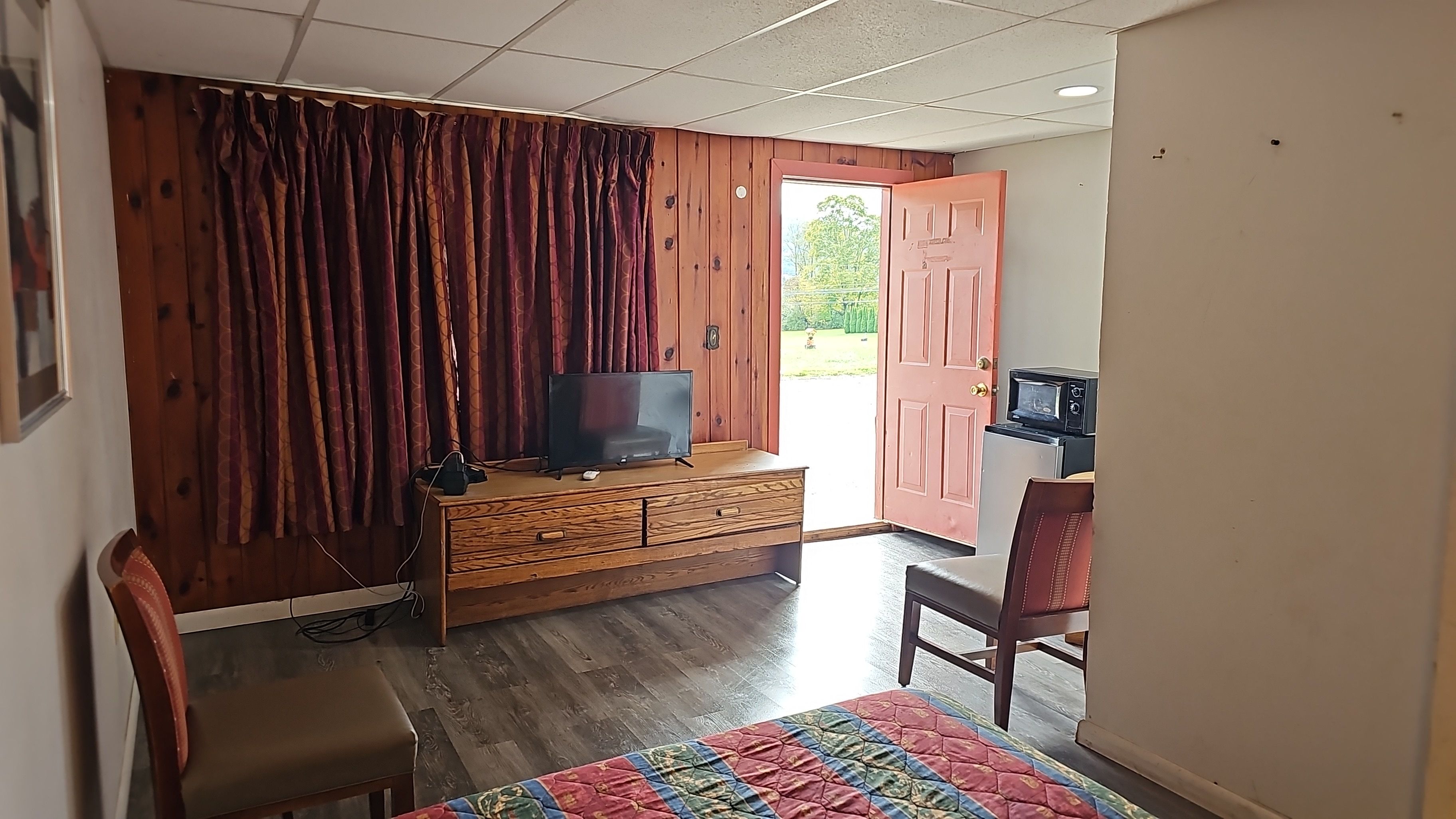 Ein Zimmer mit einem Holzkoffer, einem Fernseher, einem Sessel und einem Bett mit einer Steppdecke.