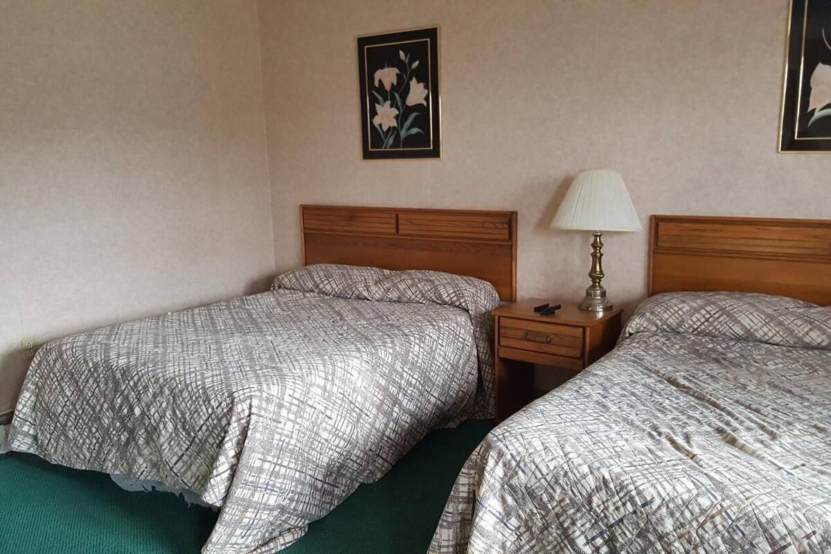 A hotel room with two beds, a nightstand with a lamp, and two framed floral pictures on the wall.