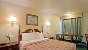 Ein Hotelzimmer mit einem Bett, zwei Nachttischlampen, einem Schreibtisch mit Stuhl und einem Fenster mit Vorhängen.