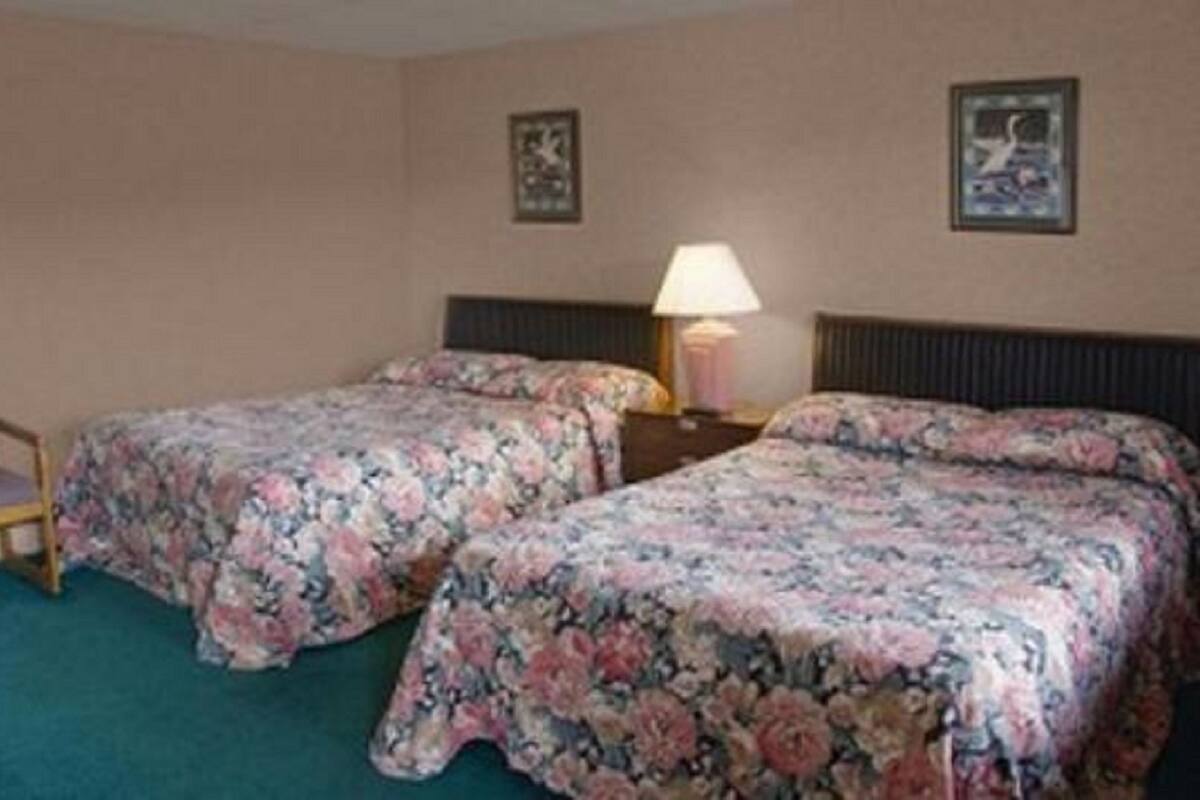 A hotel room with two beds, a chair, and a nightstand with a lamp.