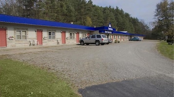A motel with a blue roof and red doors, featuring a gravel driveway and parked cars.