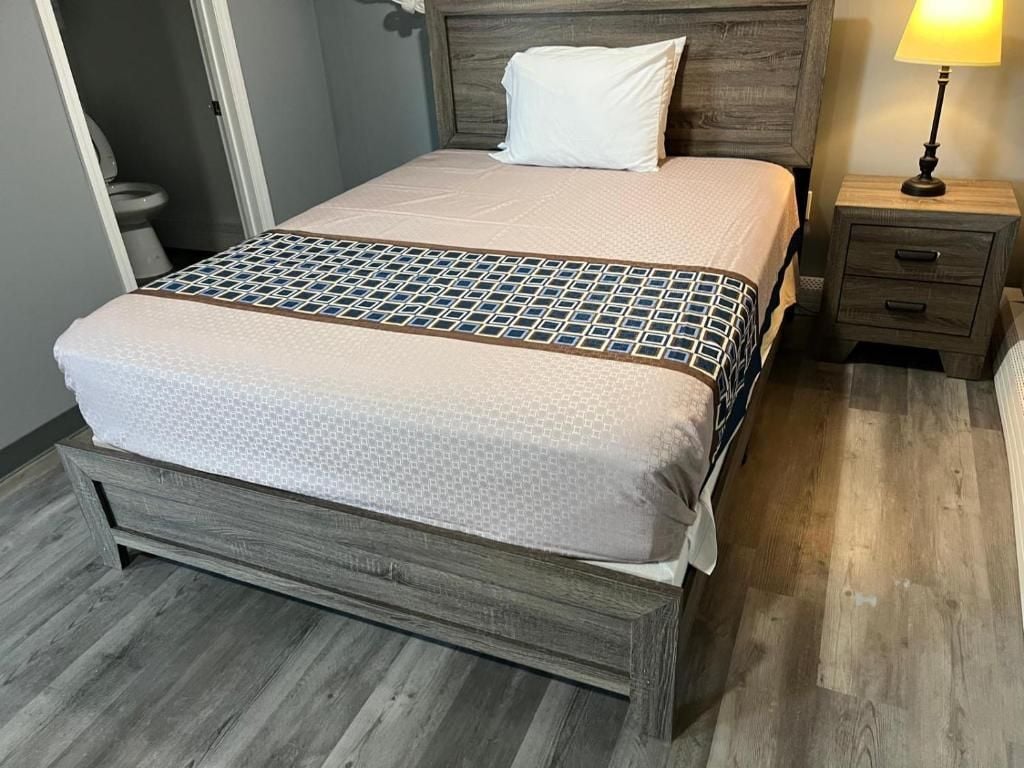 A bed with a patterned bedspread, a wooden headboard, a bedside table with drawers, and a lamp.