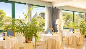 A dining area with tables set for a meal, potted plants, and a view of a building with a dome. - Hotel Sierra Silvana (Fasano)