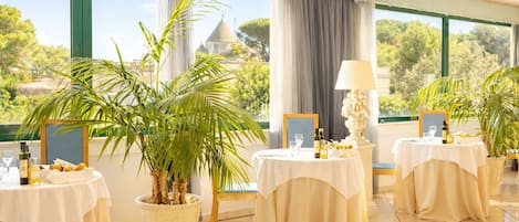A dining area with tables set for a meal, potted plants, and a view of a building with a dome.