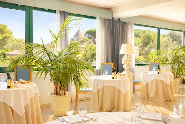 A dining area with tables set for a meal, potted plants, and a view of a building with a dome.