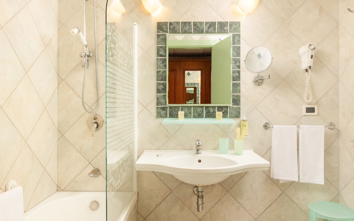 A bathroom with a glass shower enclosure, a sink with a mirror above it, a hairdryer, and a towel rack.