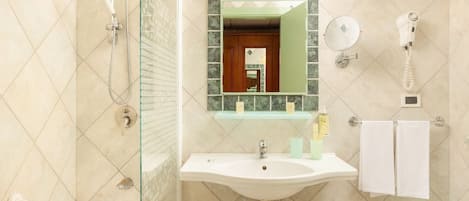 A bathroom with a glass shower enclosure, a sink with a mirror above it, a hairdryer, and a towel rack.