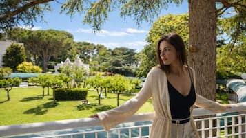 A woman standing on a balcony with a view of a park and buildings in the background.