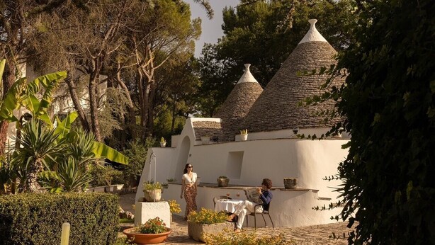 A courtyard with a white building featuring conical roofs, surrounded by greenery and potted plants. - Hotel Sierra Silvana (Fasano)