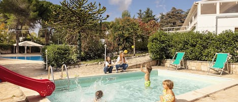 A swimming pool area with a slide, lounge chairs, and a covered seating area.