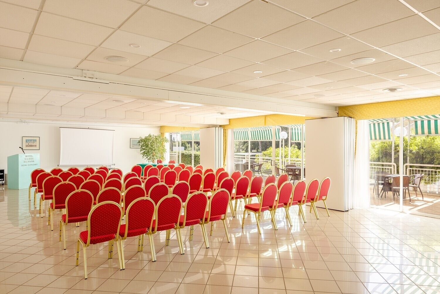 A conference room with rows of red chairs and a whiteboard, large windows, and a balcony area.