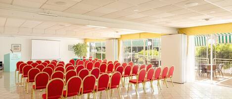 Un salón de conferencias con filas de sillas rojas, una pizarra y ventanas amplias, además de un área con balcón.