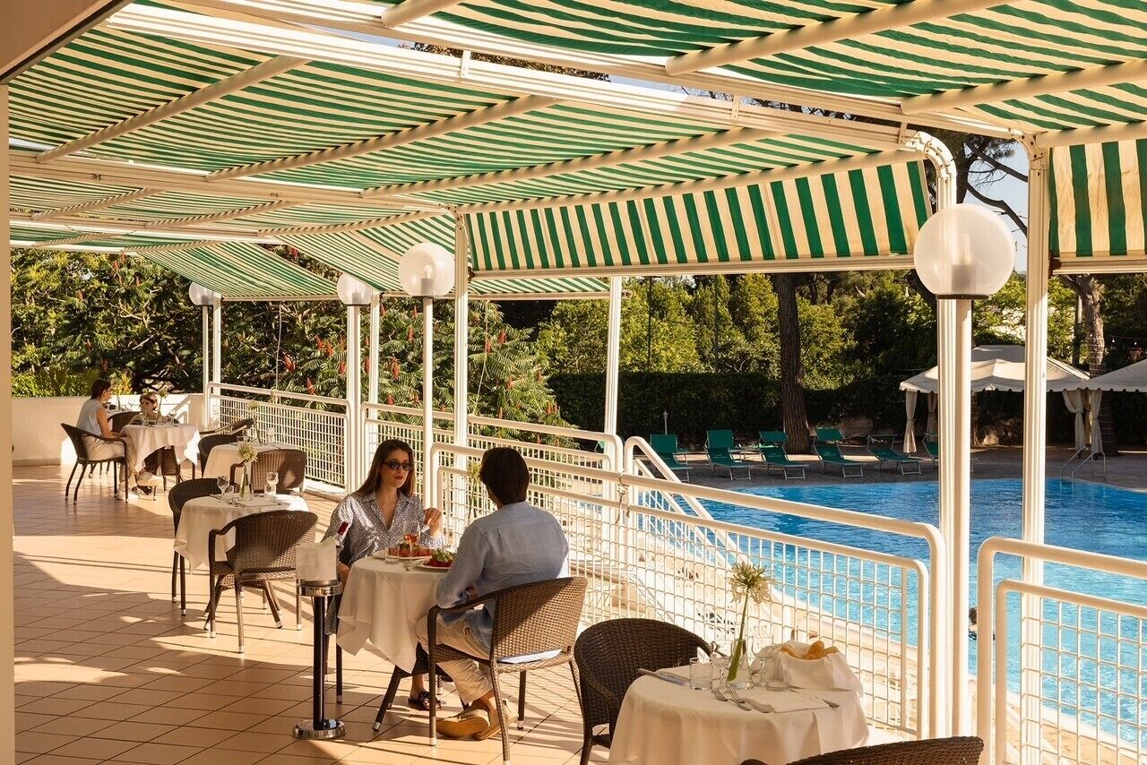 Un espacio de comedor al aire libre techado con mesas y sillas, con vistas a una piscina.