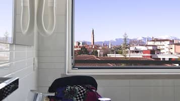 Ein Badezimmer mit einem weißen Waschbecken, einem Wasserhahn und einem Fenster mit Blick auf Gebäude und Berge.