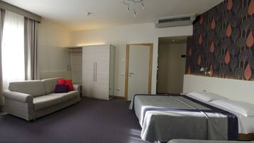 Une chambre d’hôtel avec un canapé, deux lits simples, une armoire et une porte donnant sur une autre pièce.