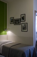 A room with a bed, a green accent wall, and four framed pictures on the wall.