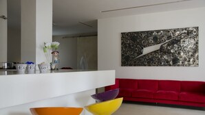 A modern living room with a red sofa, a white coffee table, and colorful bar stools. - Hotel Key (Vicenza)