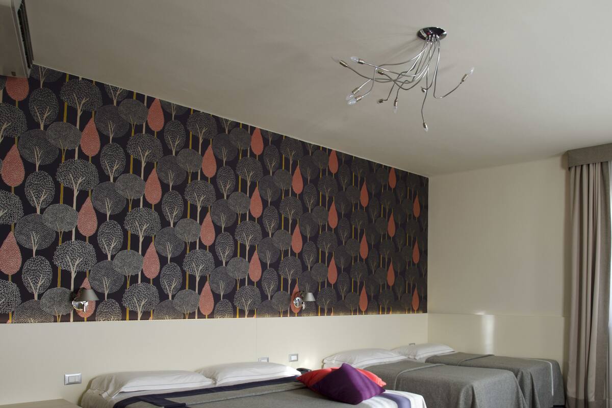 Una camera d'albergo con due letti, carta da parati decorata, un lampadario e un comodino.