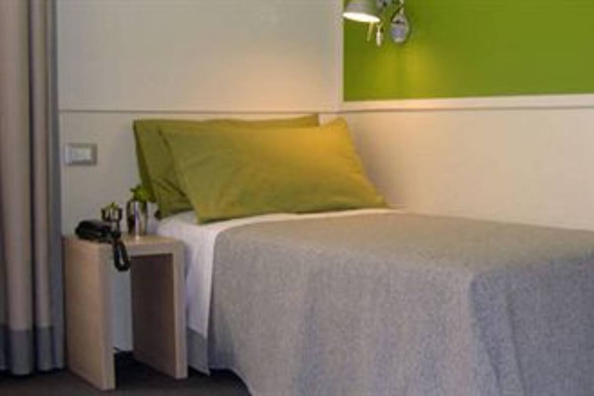 Un letto singolo con un cuscino verde, un comodino con una lampada e una sedia con un cuscino rosso.