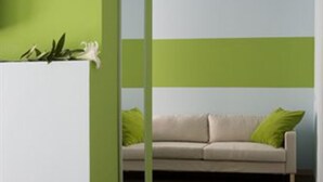 A room with a green and white color scheme, a beige sofa with green cushions, a mirror on the wall, and a bed with a green bedspread. - Hotel Key (Vicenza)