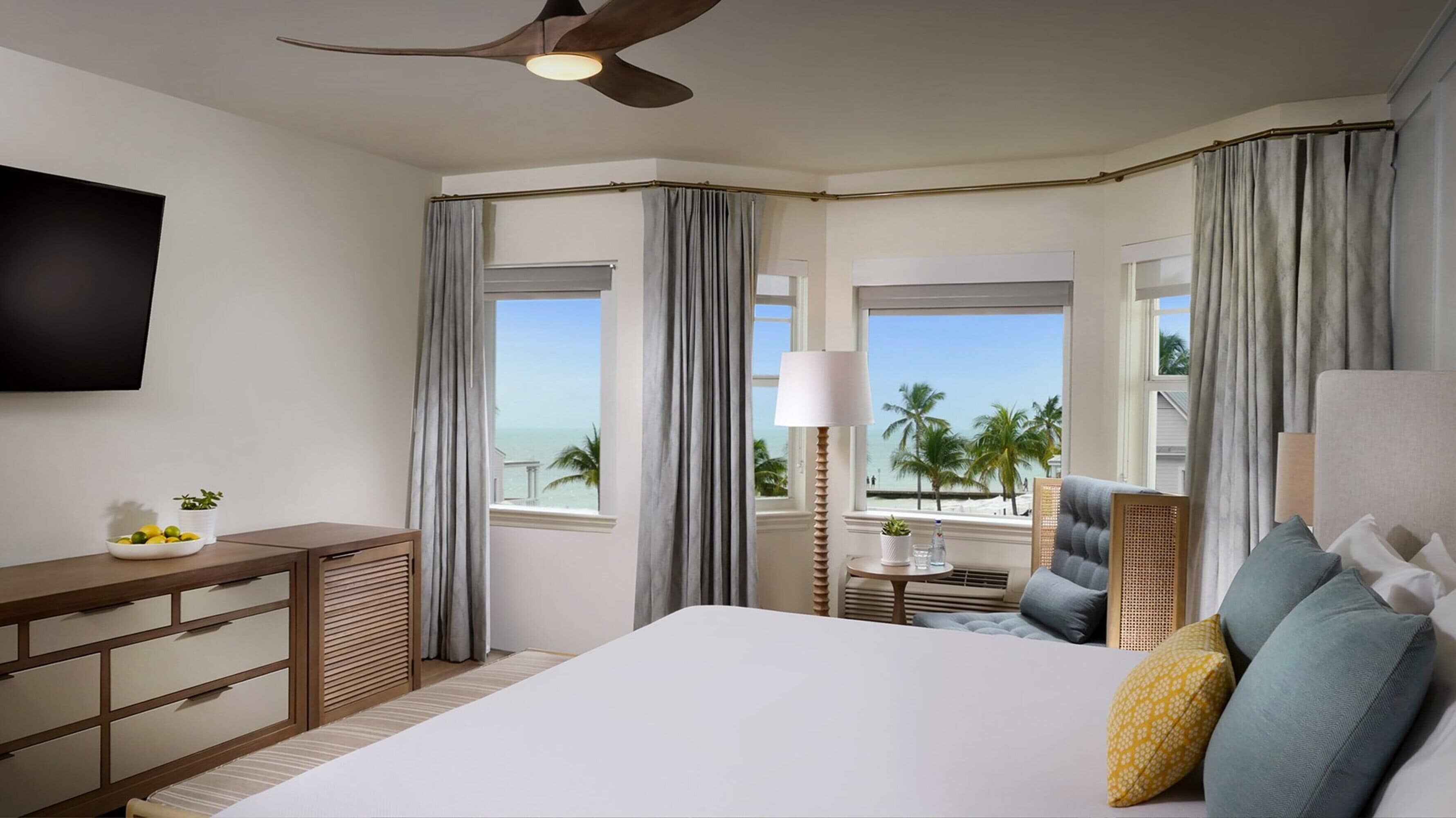 Ein Hotelzimmer mit Bett, Schreibtisch, Fernseher und Blick auf den Strand.