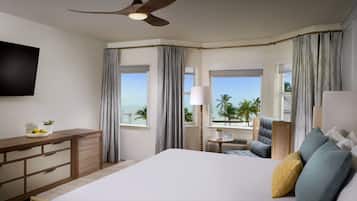 A hotel room with a bed, a desk, a TV, and a view of the beach.