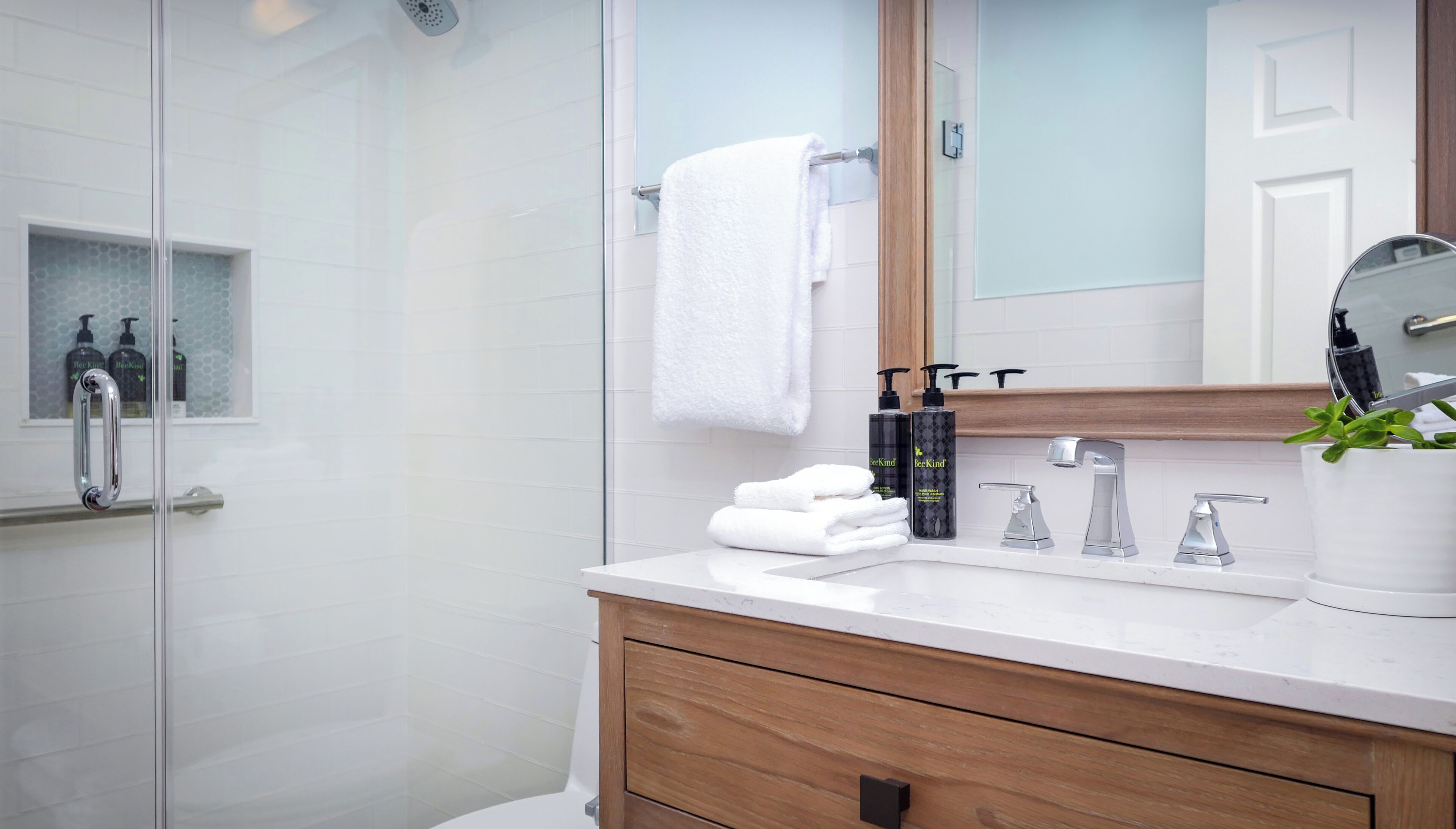 A modern bathroom with a glass shower enclosure, a white sink, a wooden vanity, and a mirror.