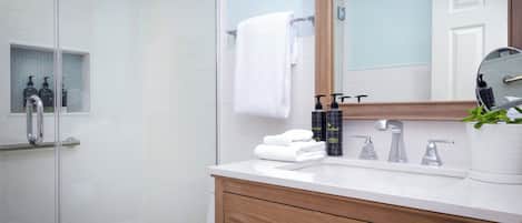 A modern bathroom with a glass shower enclosure, a white sink, a wooden vanity, and a mirror.