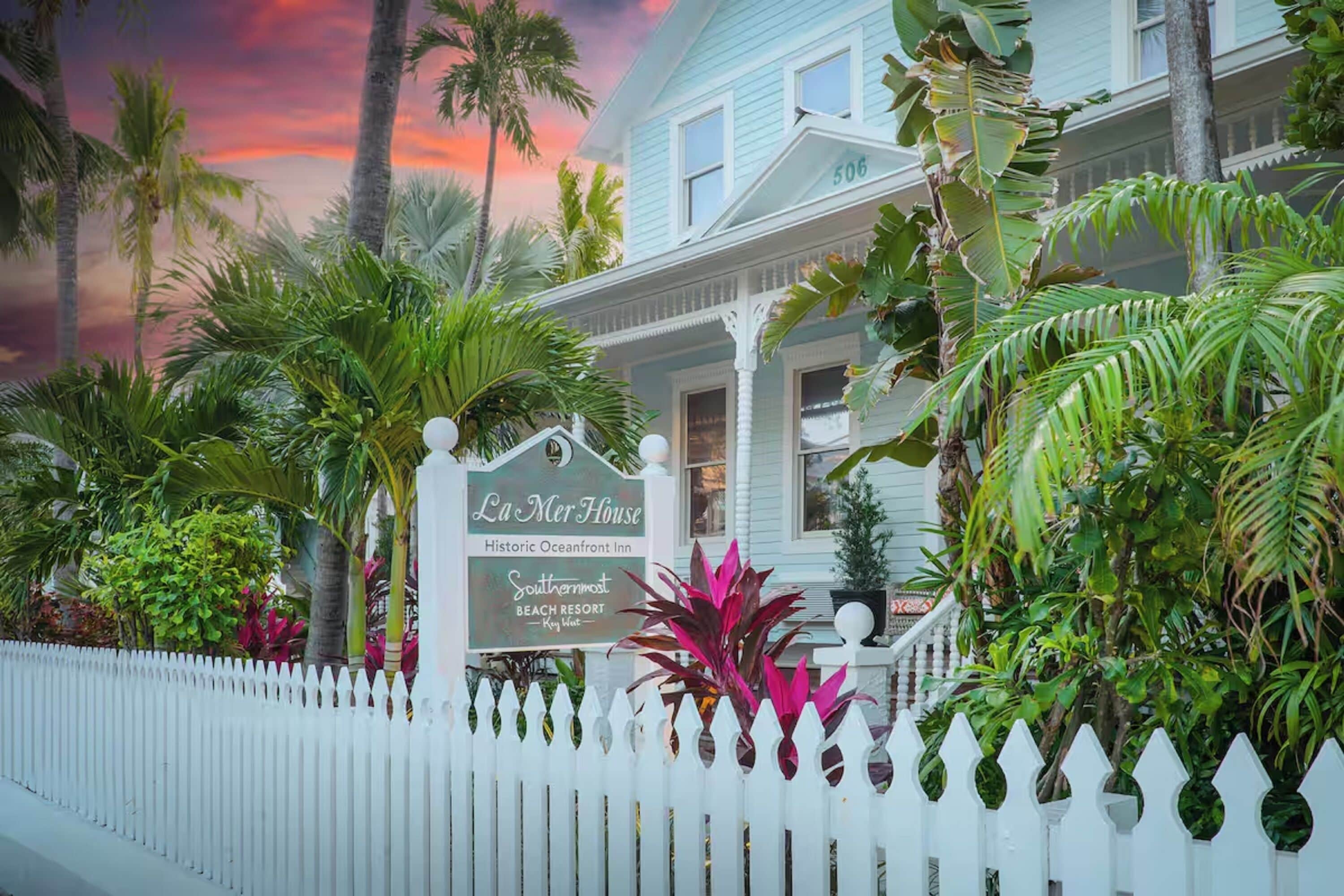 A white house with a porch, surrounded by tropical plants and palm trees, labeled "La Mer House Historic Oceanfront Inn Southernmost Beach Resort Key West."