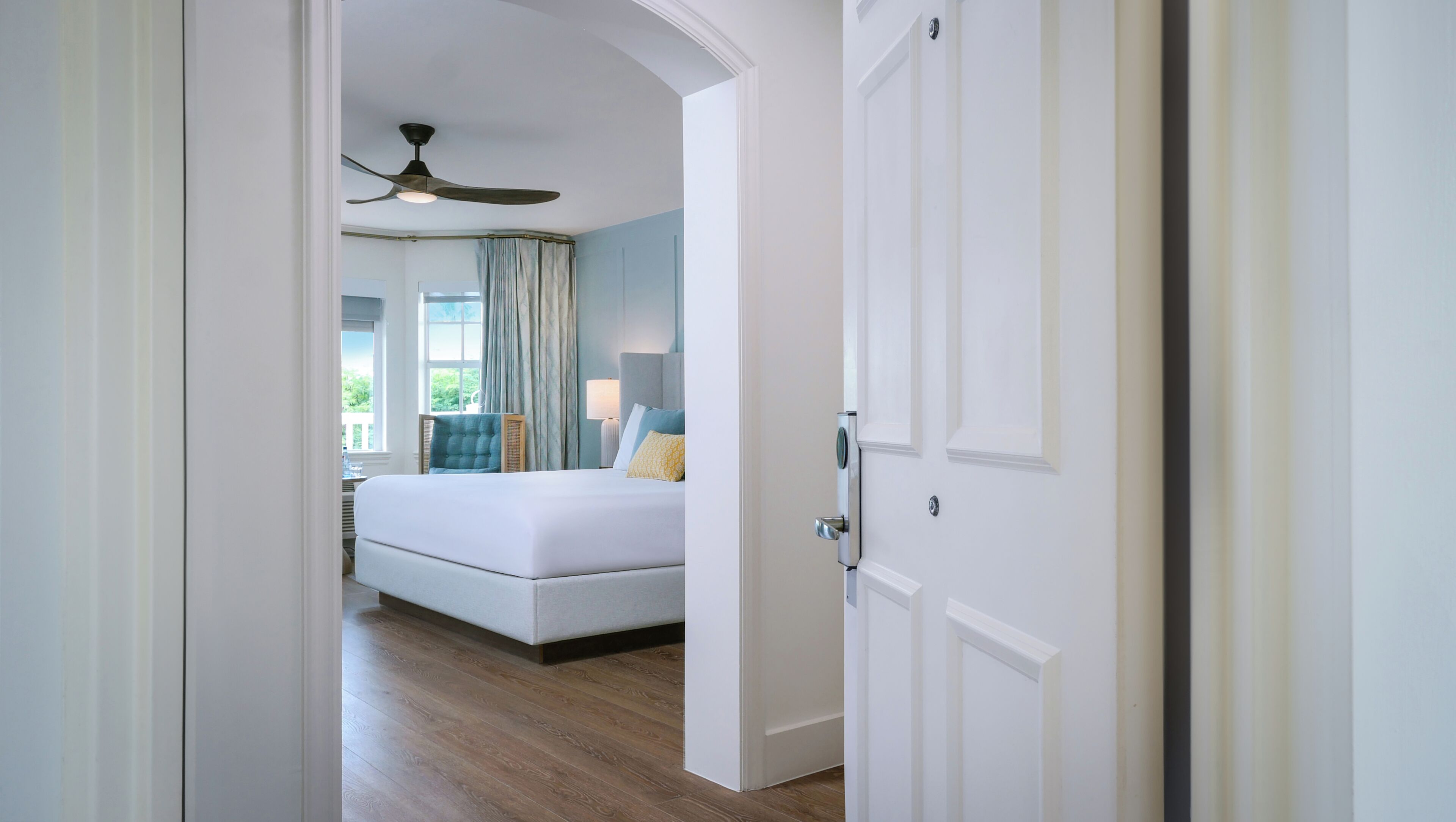 A bedroom with a bed, a ceiling fan, a window with curtains, and a view of greenery outside.