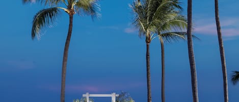 Decoración para boda al aire libre con un arco blanco y sillas dispuestas en filas mirando al océano.