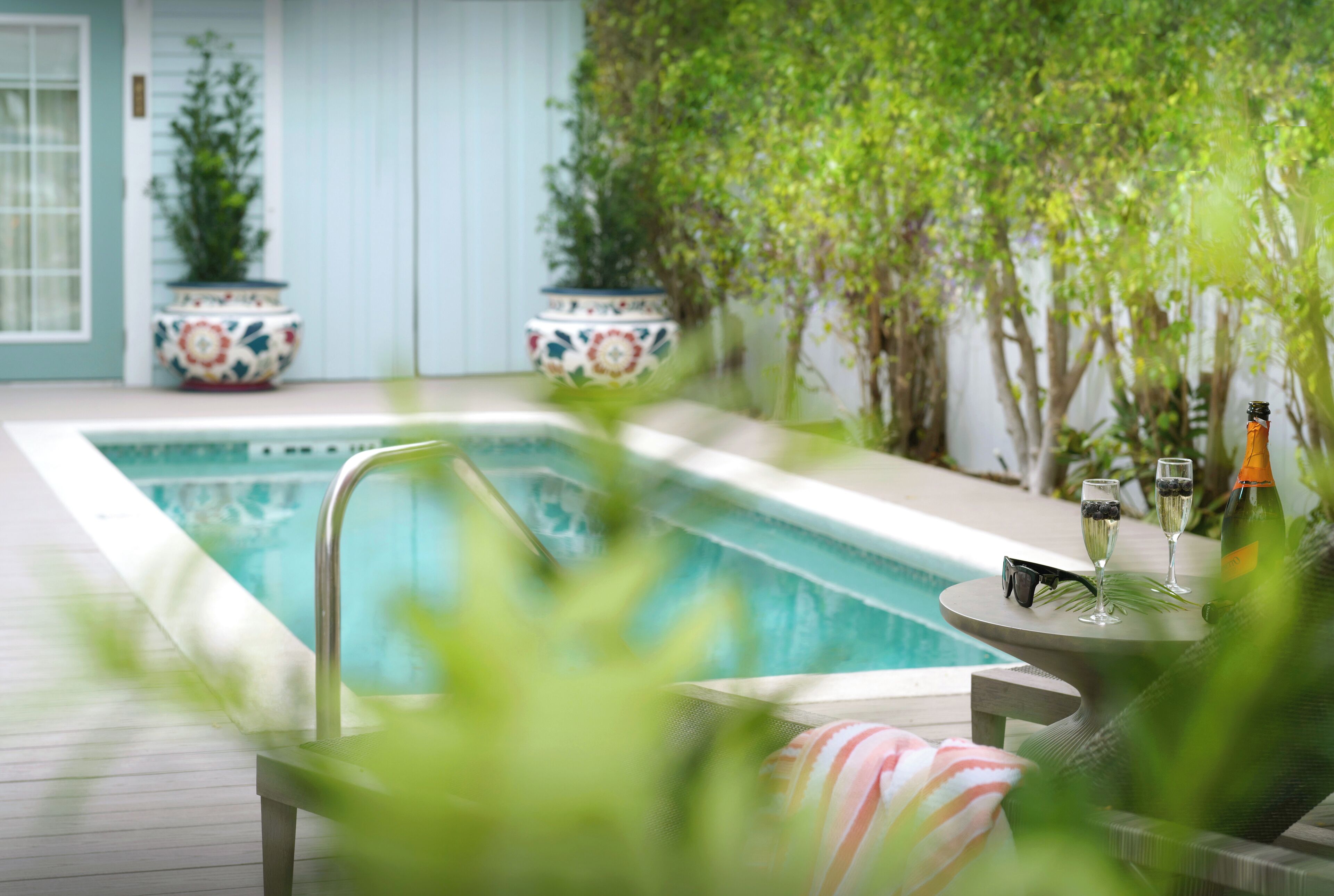 A poolside area with a pool, lounge chairs, and potted plants.