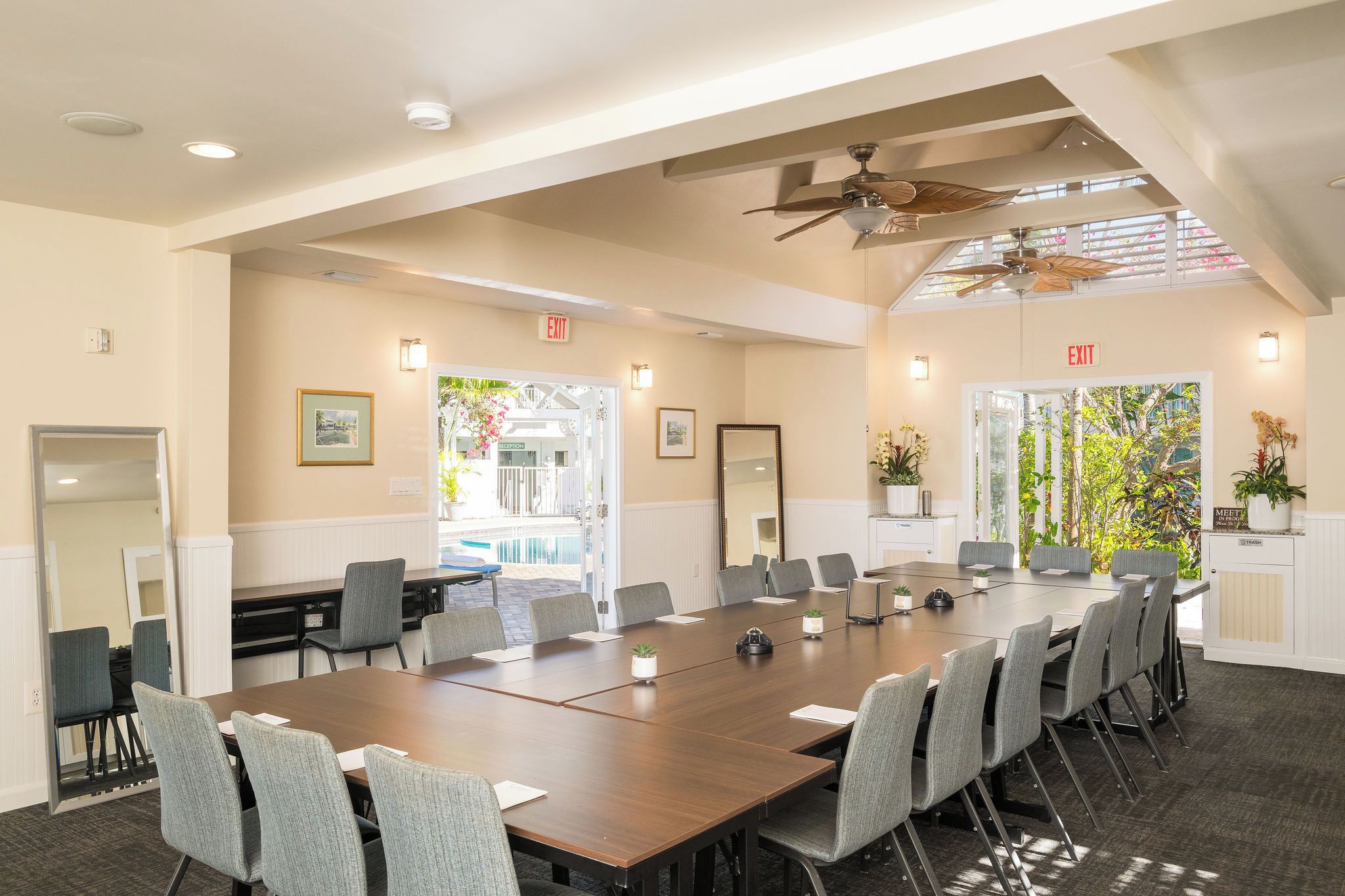 A conference room with a long table, chairs, ceiling fans, and exit signs.