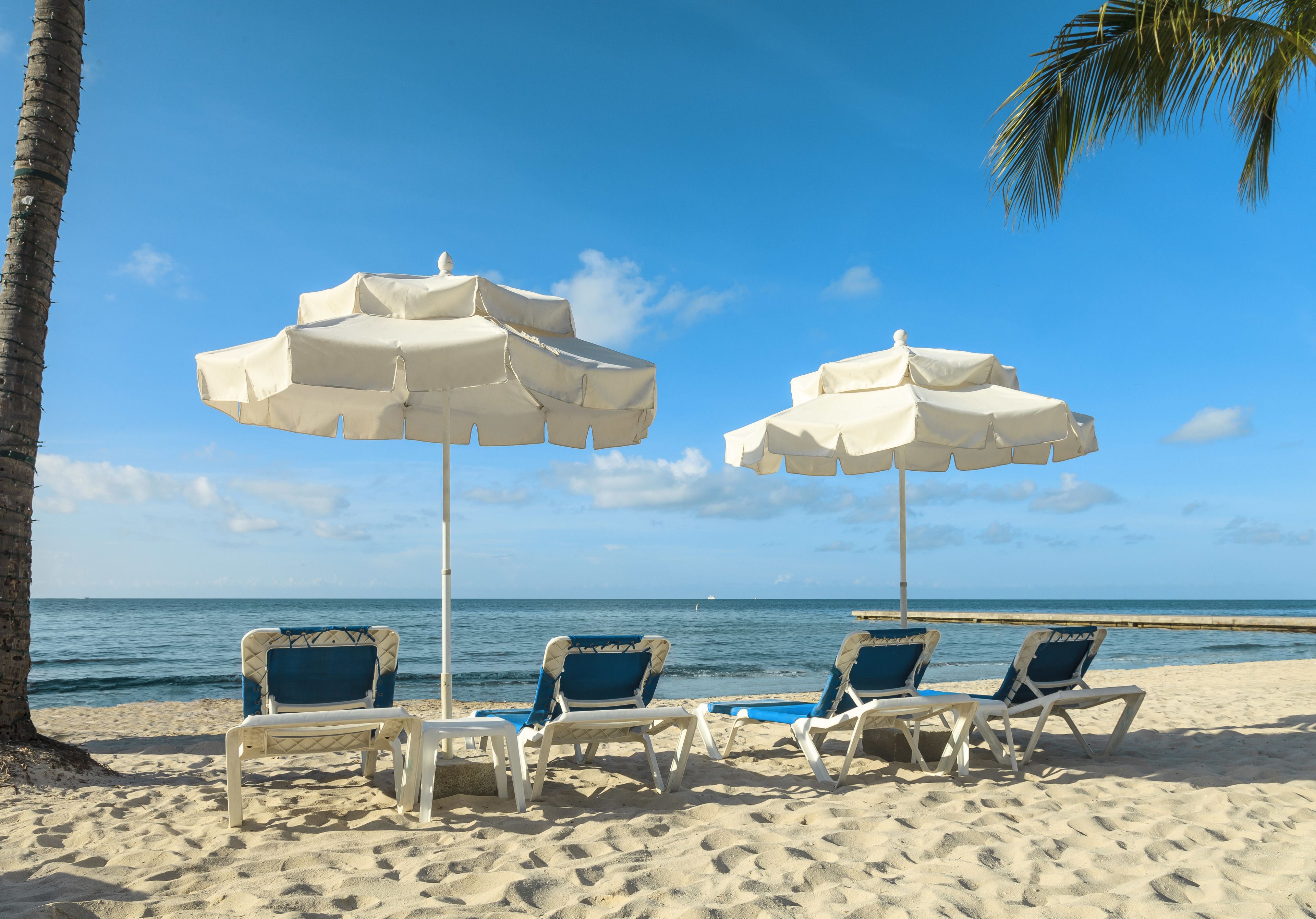 A beach with two white umbrellas and blue chairs.